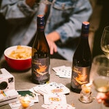 Image of bottle of wine with camera, cards and crisps